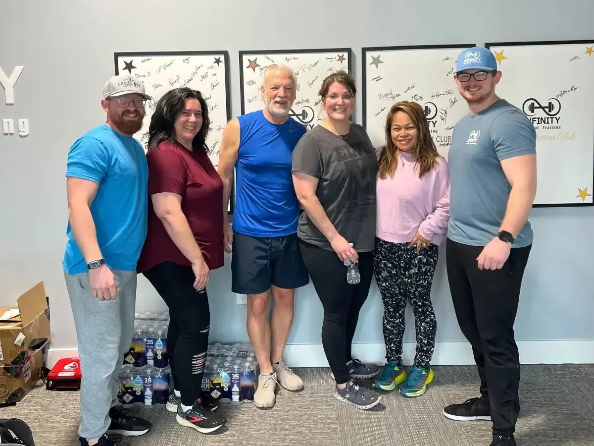 Group of six people posing in a gym setting with water bottles and fitness-themed decor