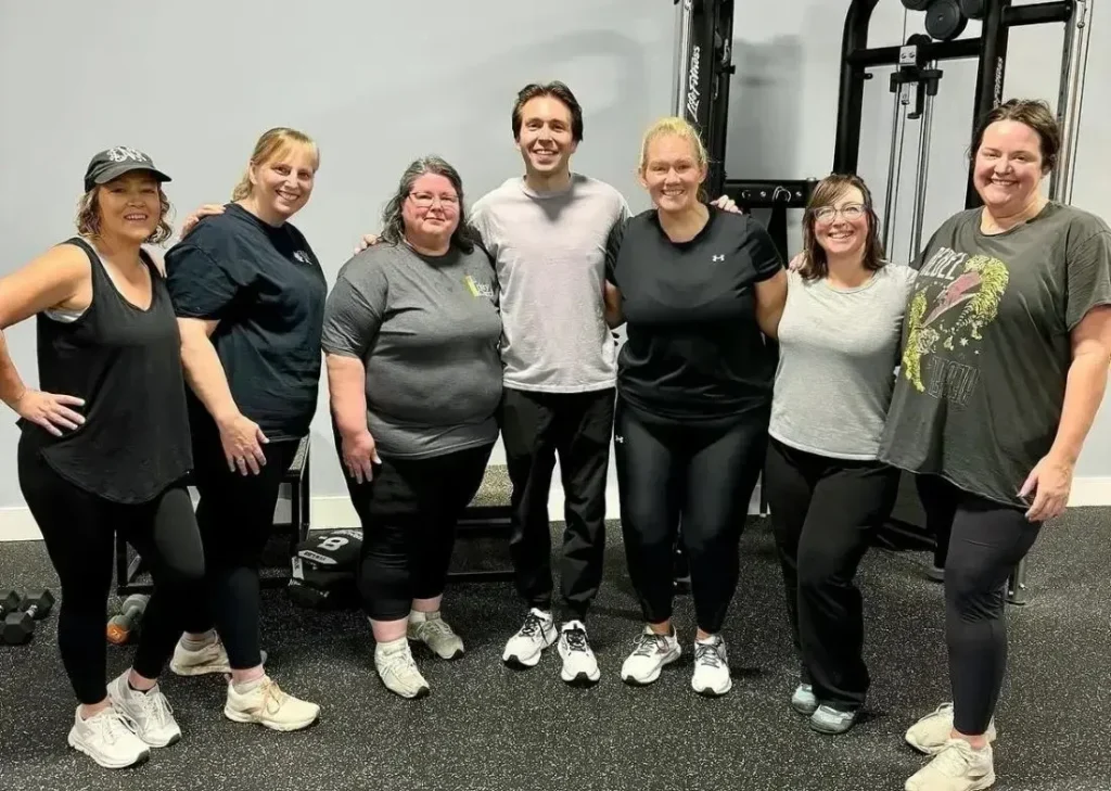 Group of seven women and one man smiling in a gym setting