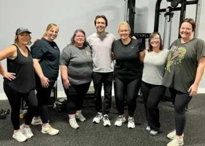 Group of seven women and one man smiling in a gym setting